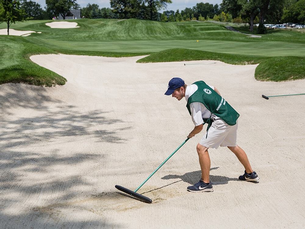 Evans Scholar caddy raking a bunker