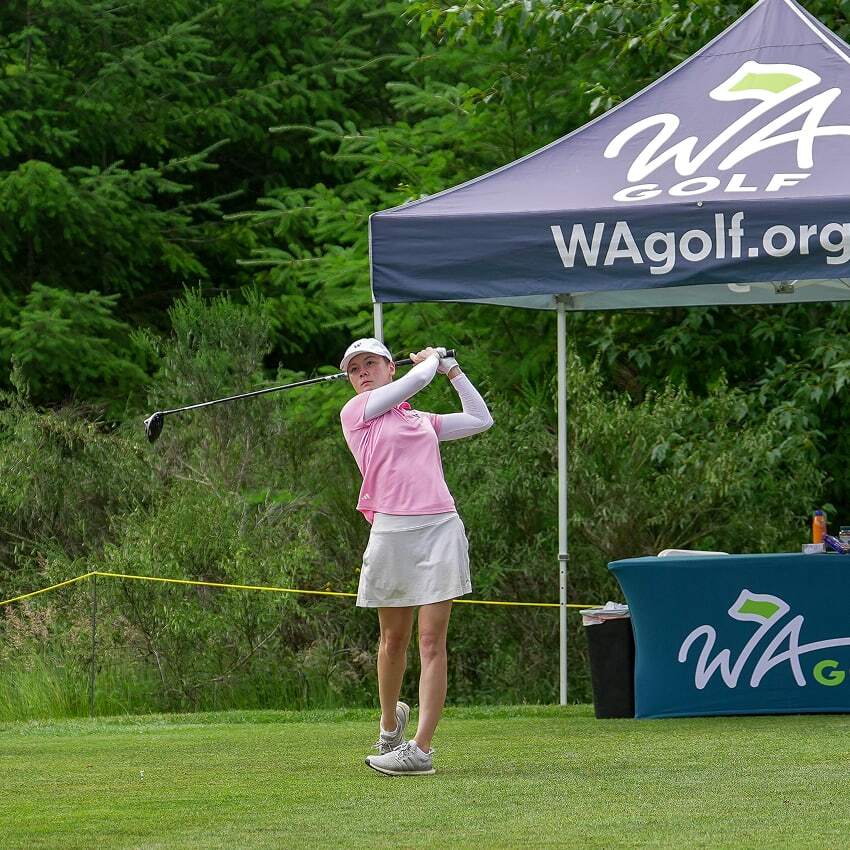 Golfer hits an iron shot during a WA Golf championship, with a WA Golf tent visible in the background