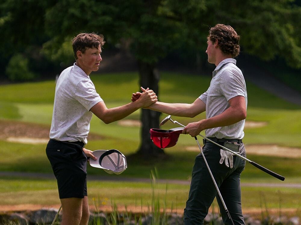 Two golfers shake hands on the green following a tournament round.